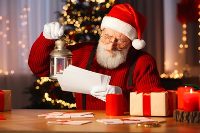 Photo of Santa Claus holding lantern and reading letters at his workplace in room decorated for Christmas