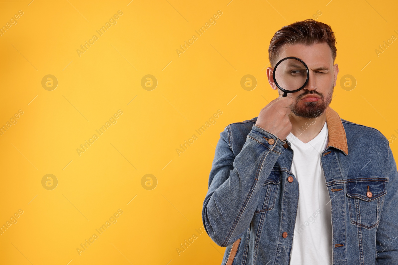 Photo of Handsome man looking through magnifier on yellow background. Space for text