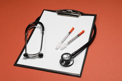 Photo of Stethoscope, syringes and clipboard on crimson background. Medical tools