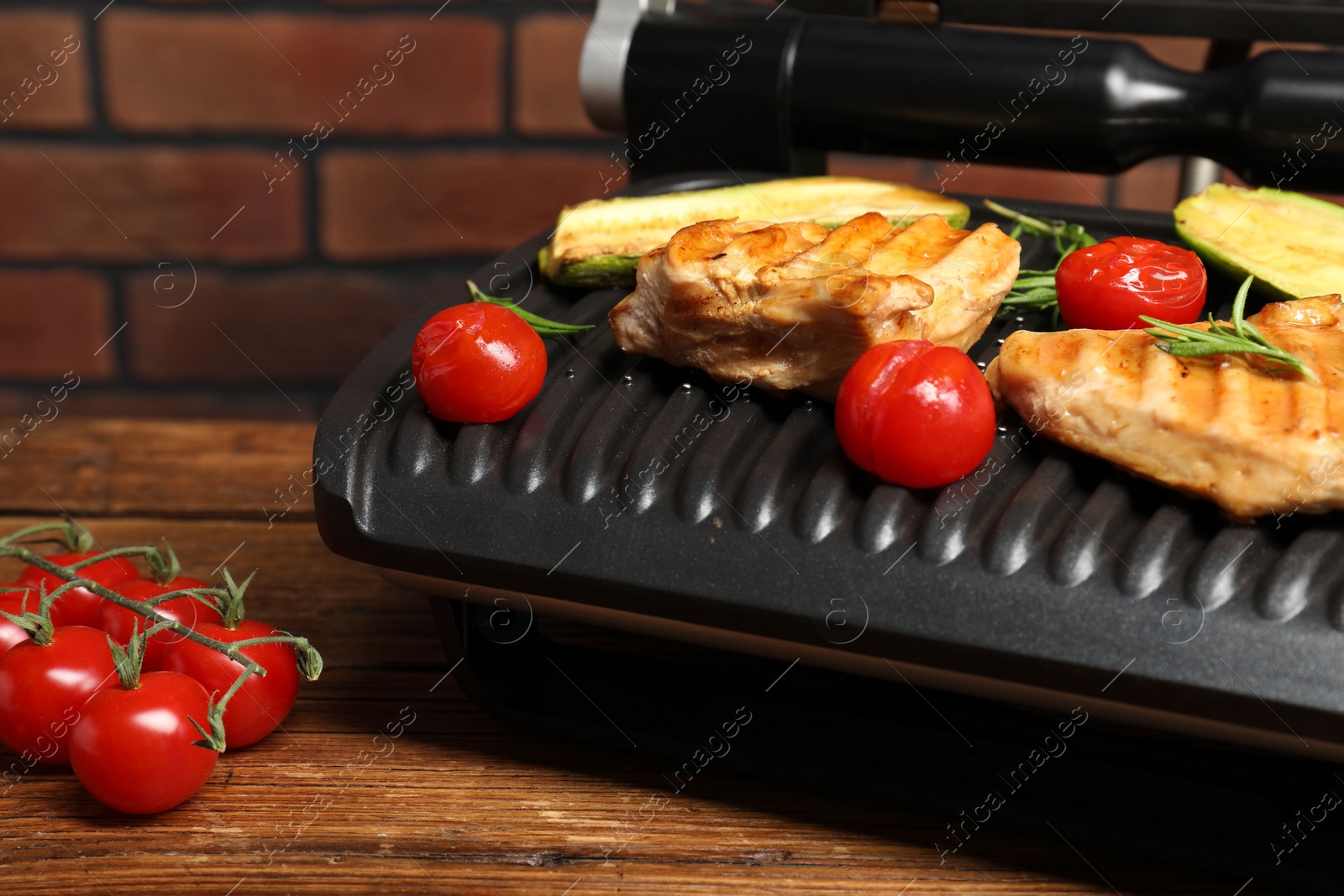 Photo of Electric grill with tasty meat, rosemary and vegetables on wooden table, closeup