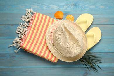 Photo of Beach towel, flip flops and hat on light blue wooden background, flat lay