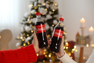 MYKOLAIV, UKRAINE - January 01, 2021: Women with bottles of Coca-Cola against blurred Christmas tree, closeup