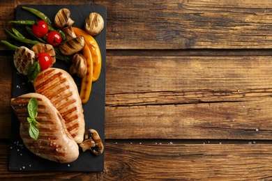 Photo of Tasty grilled chicken fillets with vegetables on wooden table, flat lay. Space for text
