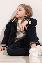 Fashion concept. Stylish girl sitting near white wall