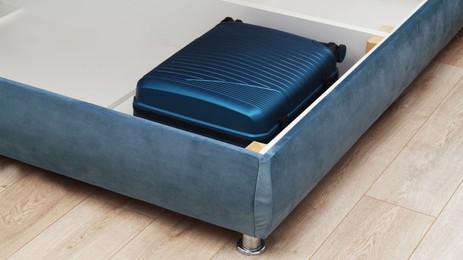 Storage drawer under bed with blue suitcase indoors