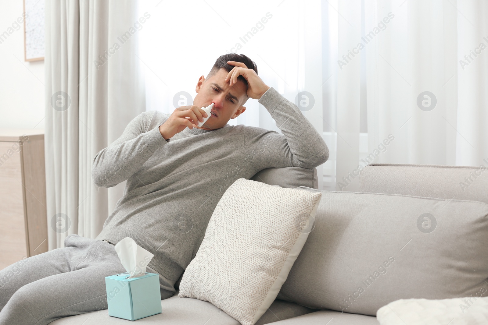 Photo of Ill man using nasal spray on sofa at home