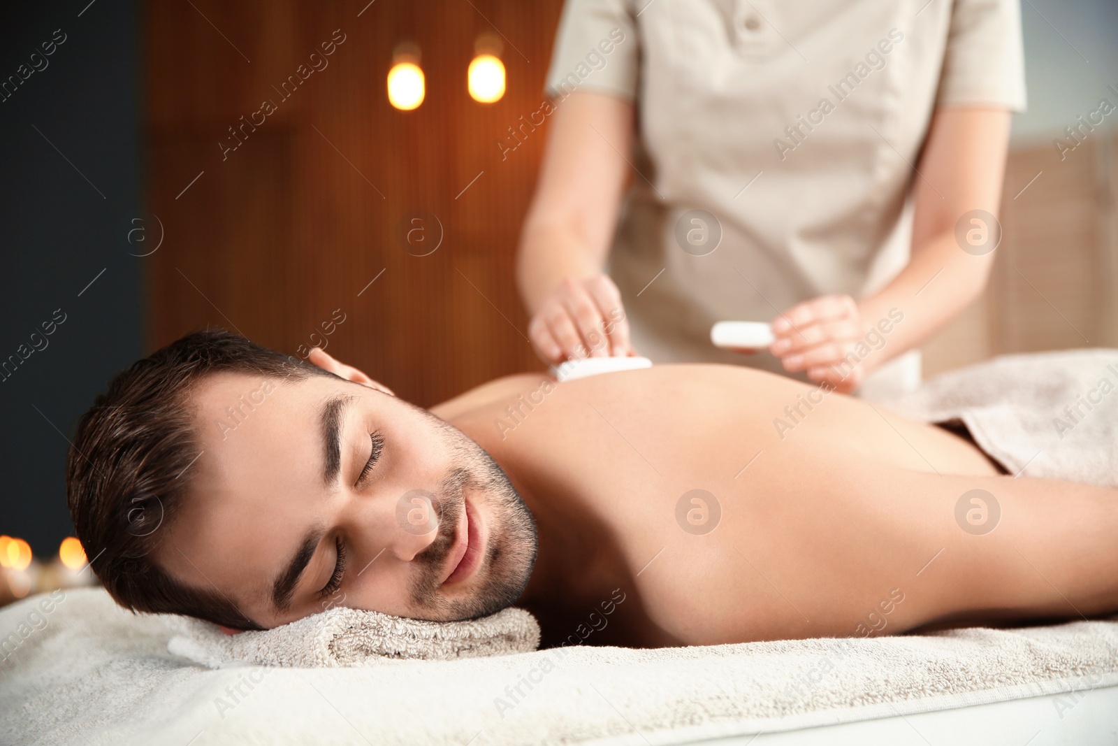 Photo of Handsome man receiving hot stone massage in spa salon