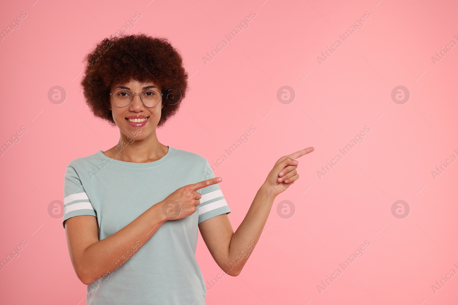 Photo of Happy young woman pointing at something on pink background. Space for text