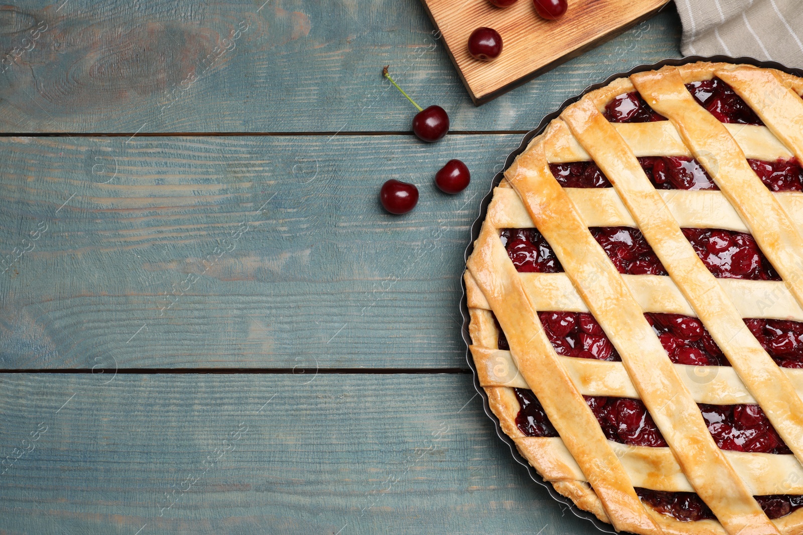 Photo of Delicious fresh pie and cherries on light blue wooden table, flat lay. Space for text