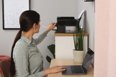 Woman using modern printer at workplace indoors