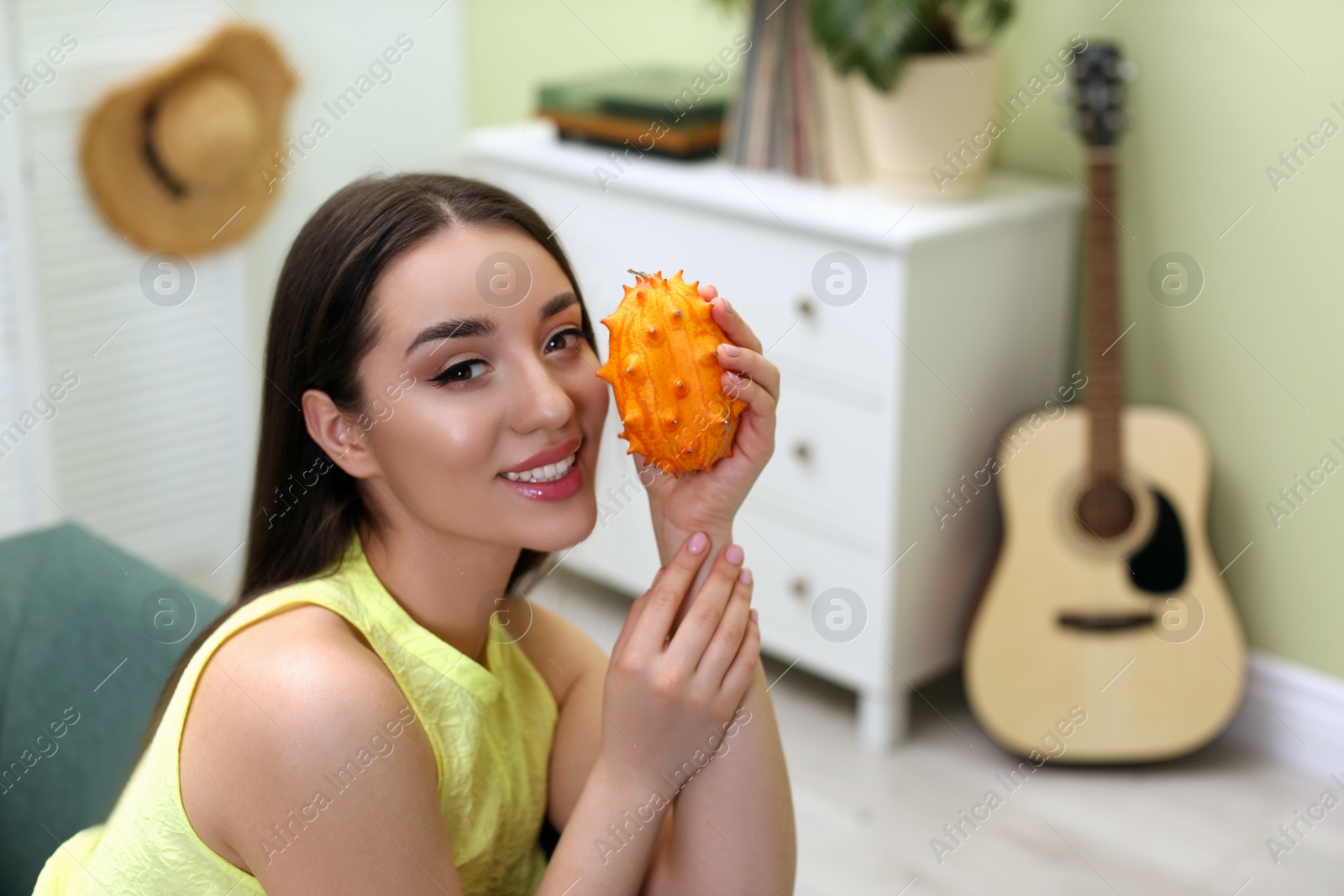 Photo of Young woman with fresh kiwano at home, space for text. Exotic fruit