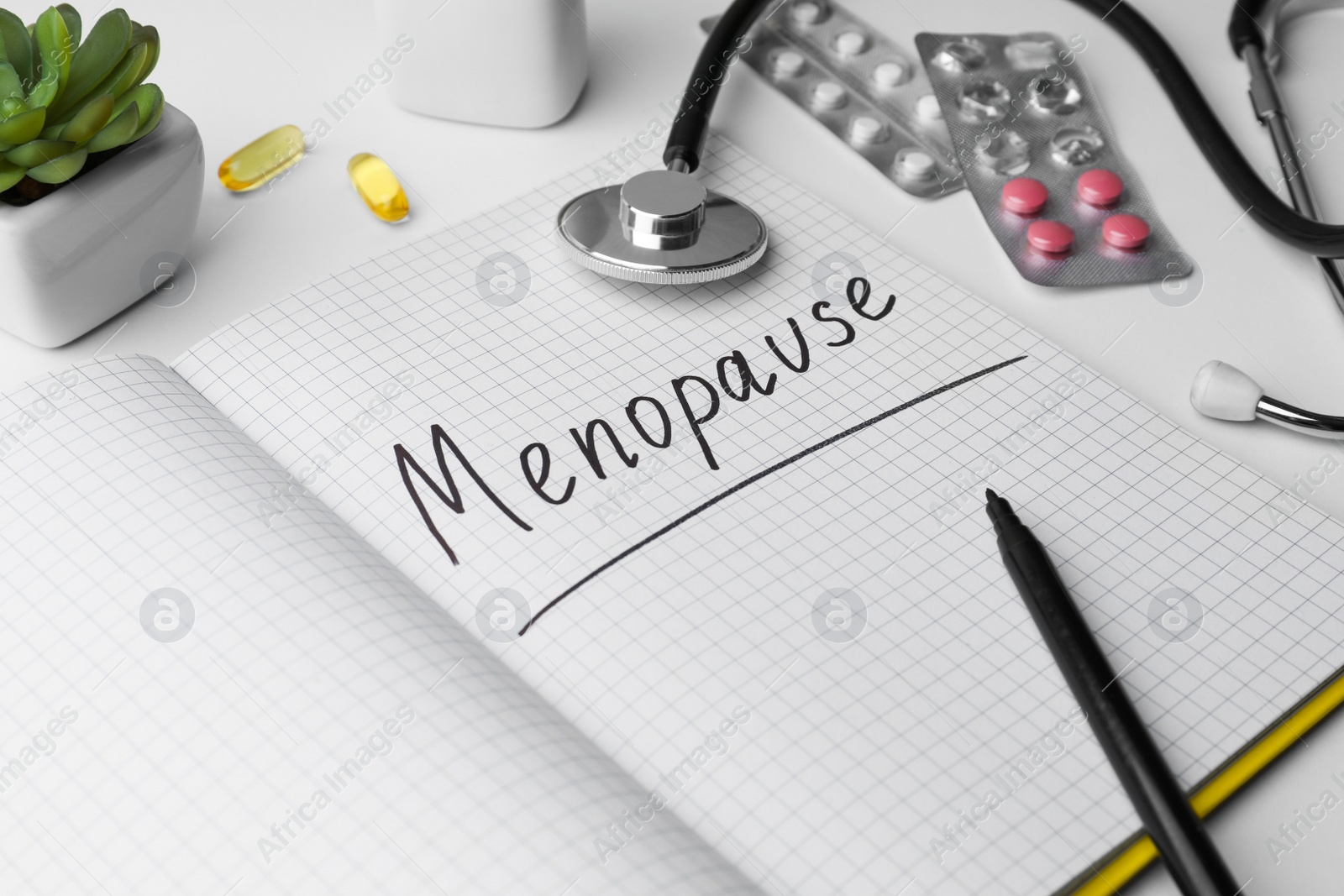 Photo of Notebook with word Menopause, stethoscope, pills and houseplant on white background, closeup