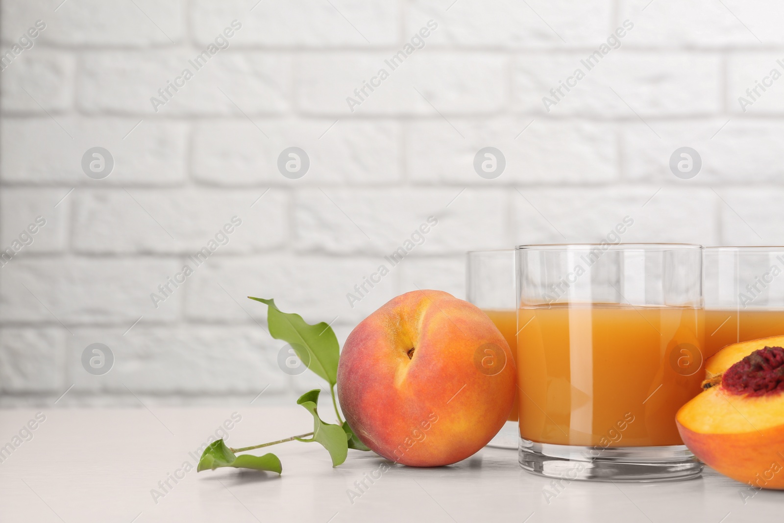 Photo of Glasses of delicious peach juice and fresh fruits on white wooden table. Space for text