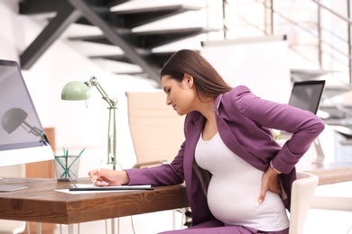 Young pregnant woman suffering from pain while working in office