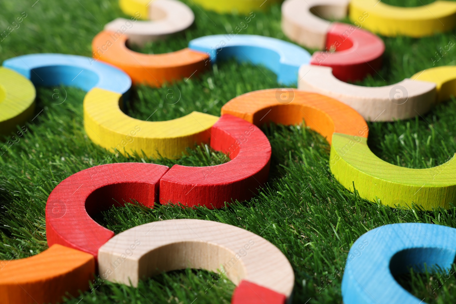 Photo of Colorful wooden pieces of play set on green grass, closeup. Educational toy for motor skills development