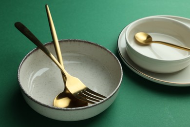 Stylish empty dishware and golden cutlery on green background