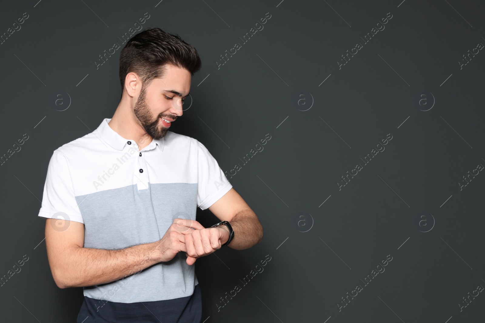 Photo of Portrait of handsome man looking at wristwatch on grey background