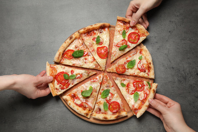 People taking slices of delicious pizza Margherita at grey table, top view