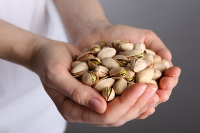 Photo of Woman holding handful of tasty pistachios on grey background, closeup