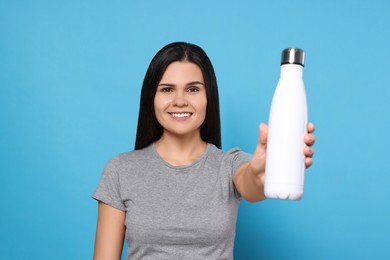 Young woman with thermo bottle on light blue background
