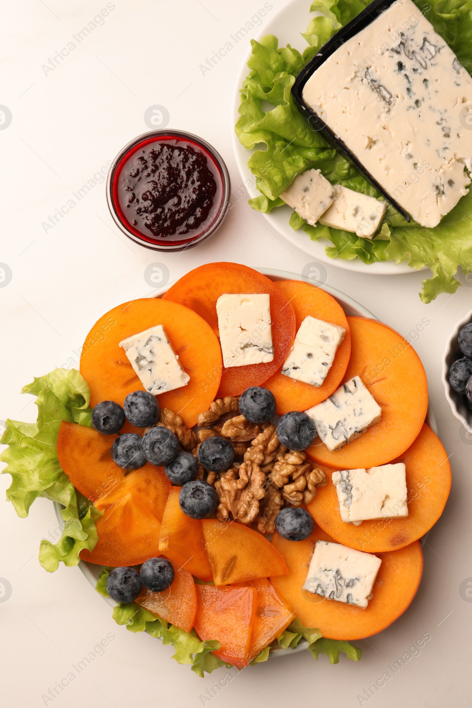 Photo of Delicious persimmon with blue cheese on white marble table, flat lay