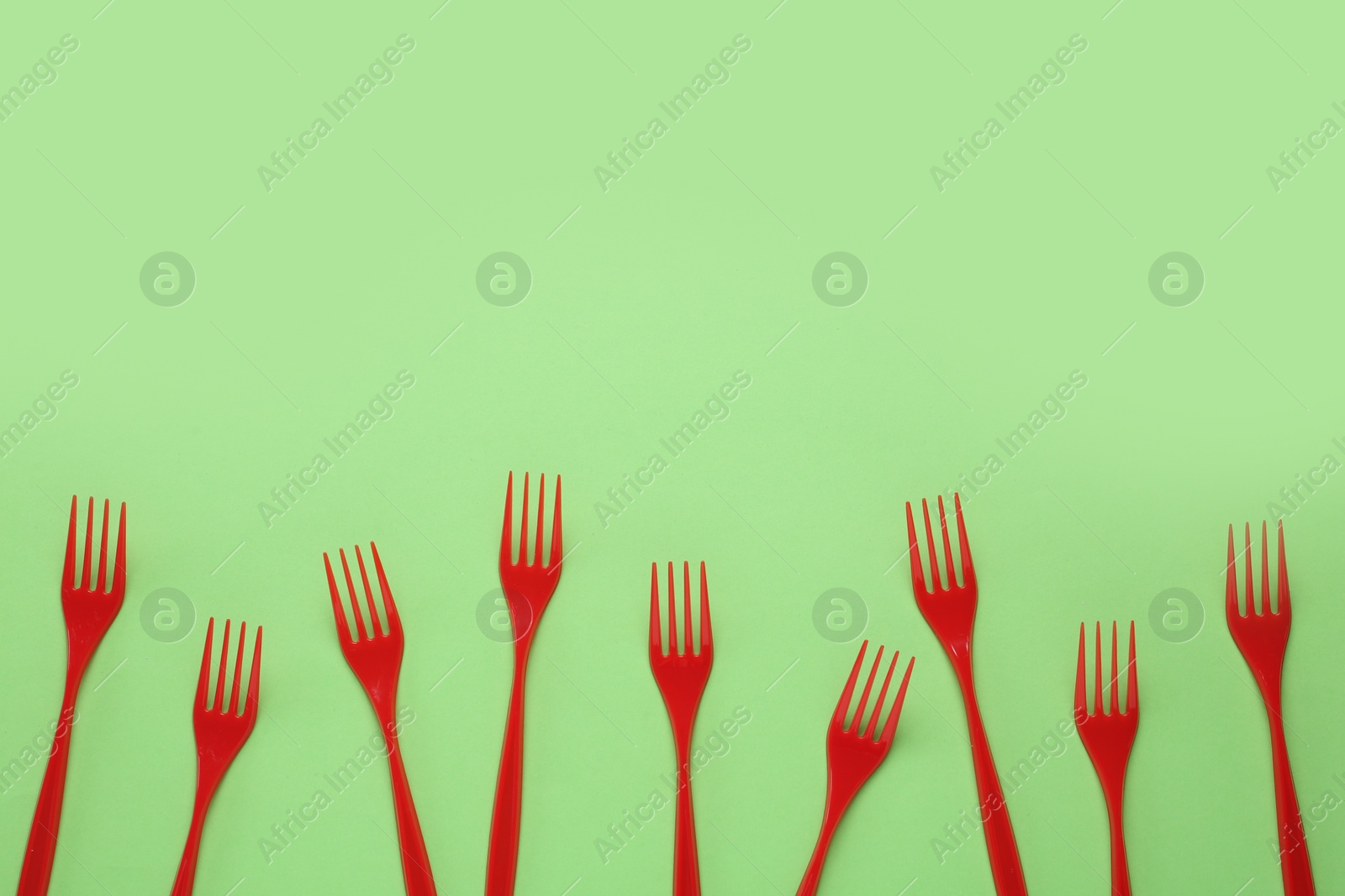 Photo of Plastic forks on green background, flat lay. Space for text