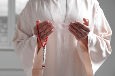 Photo of Muslim man with misbaha praying indoors, closeup