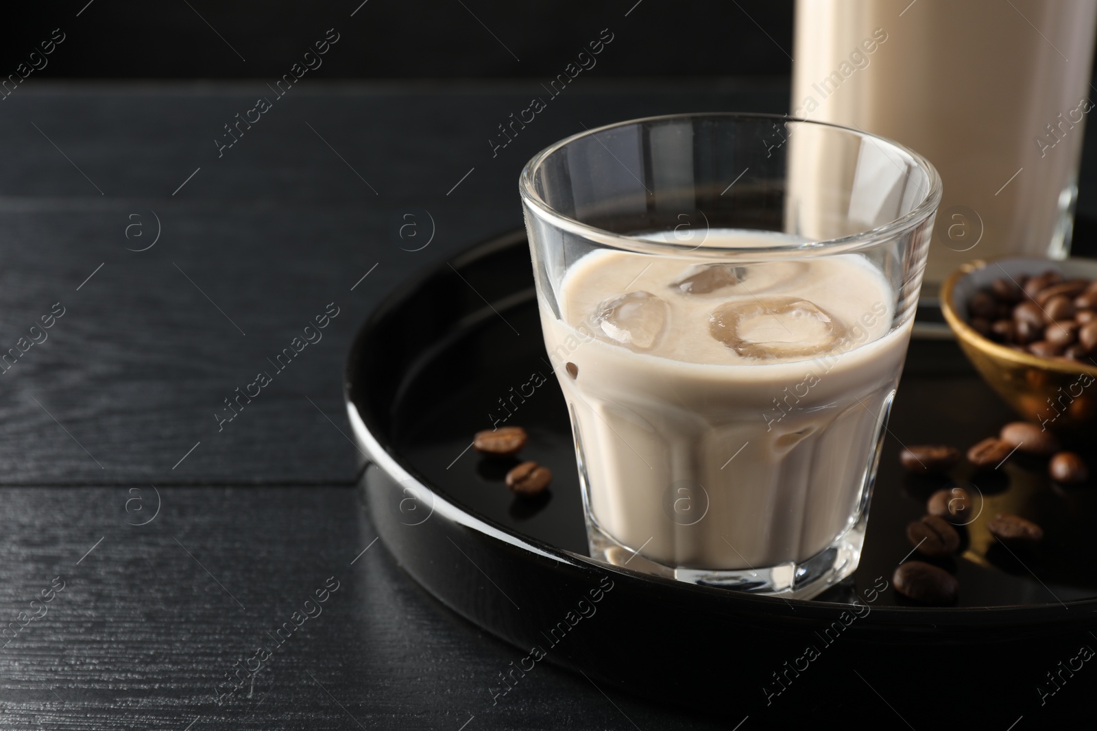 Photo of Coffee cream liqueur in glass and beans on black wooden table, space for text