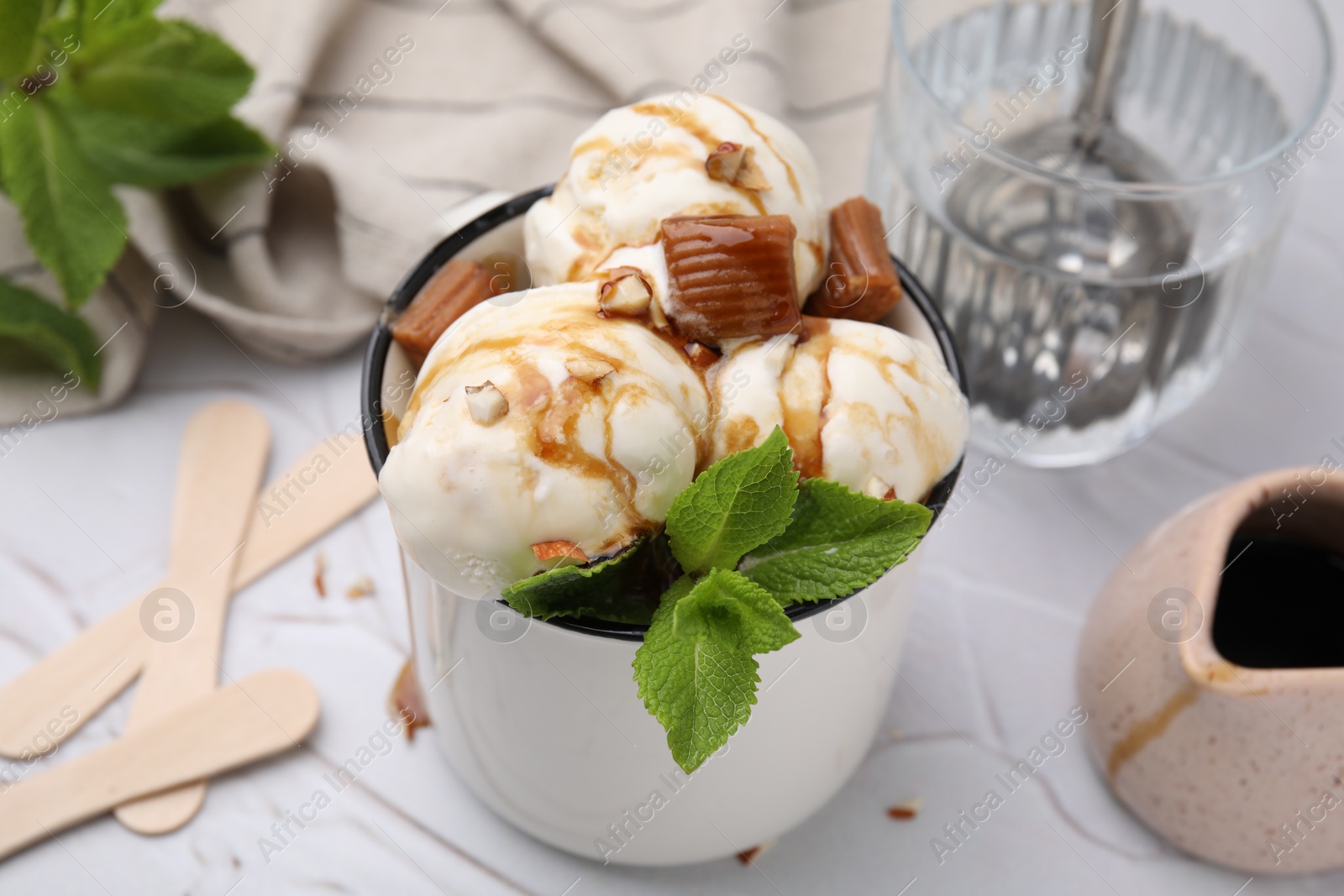 Photo of Scoops of ice cream with caramel sauce, candies and mint leaves on white textured table, closeup