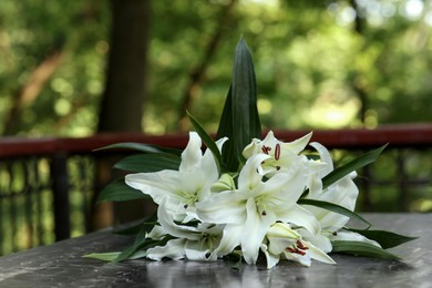 Photo of White lilies on tombstone at cemetery outdoors. Funeral ceremony