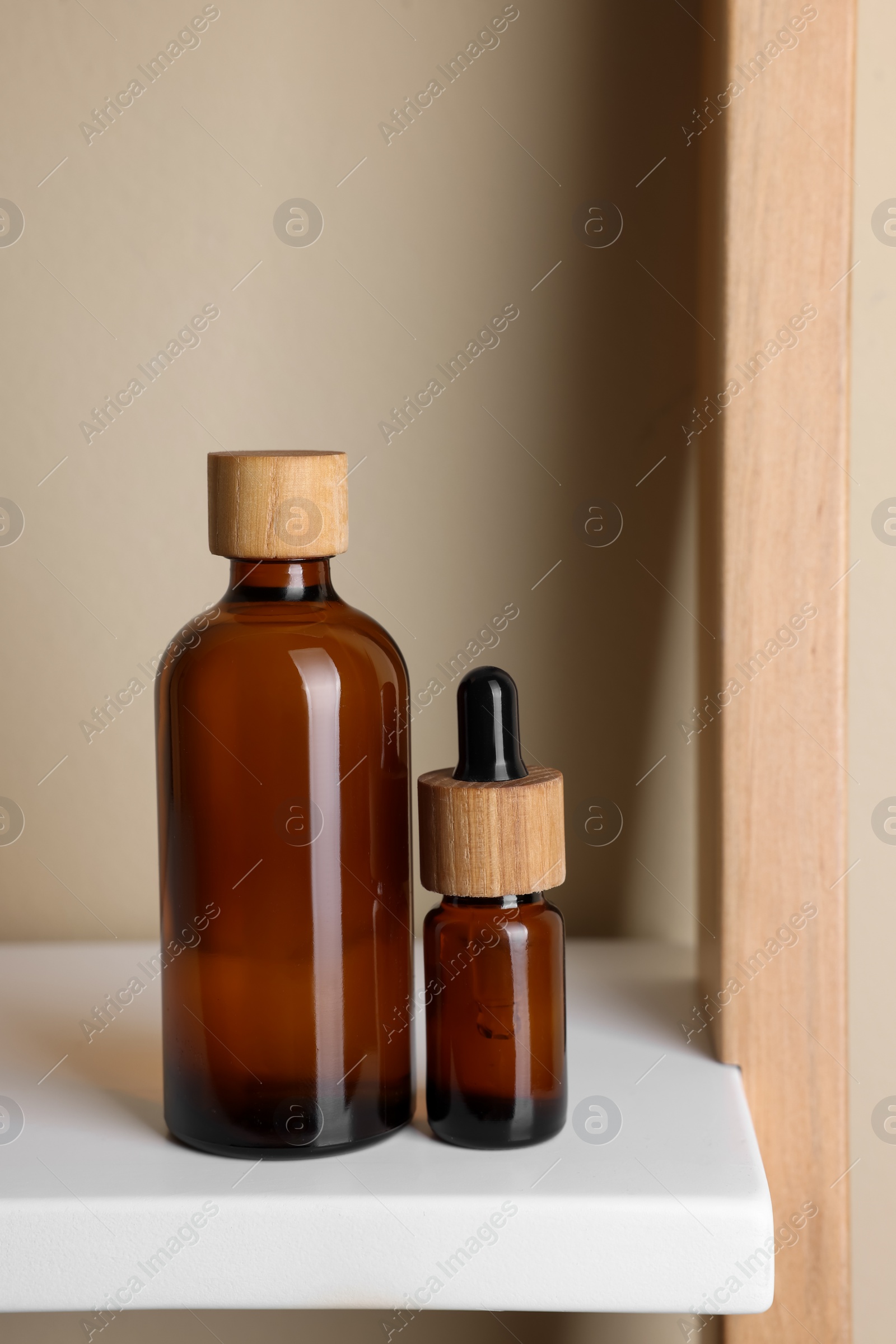 Photo of Glass bottles of cosmetic products on white shelf