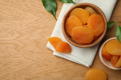 Tasty apricots with bowl on wooden table, flat lay and space for text. Dried fruits