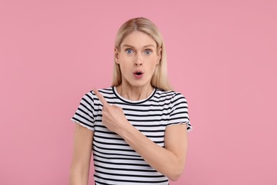 Surprised woman pointing at something on pink background