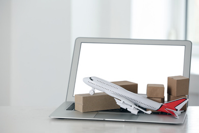 Photo of Laptop and plane model with boxes on table indoors. Courier service