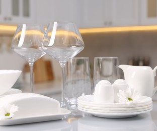 Photo of Set of clean dishware, glasses and flowers on table in kitchen