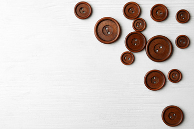 Many brown sewing buttons on white wooden background, flat lay. Space for text