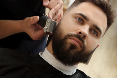 Photo of Professional hairdresser working with client in barbershop, closeup