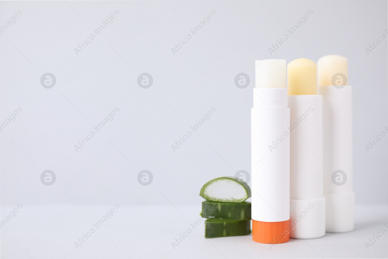 Photo of Hygienic lipsticks and cut aloe vera leaf on light table, space for text