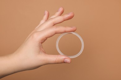Photo of Woman holding diaphragm vaginal contraceptive ring on light brown background, closeup