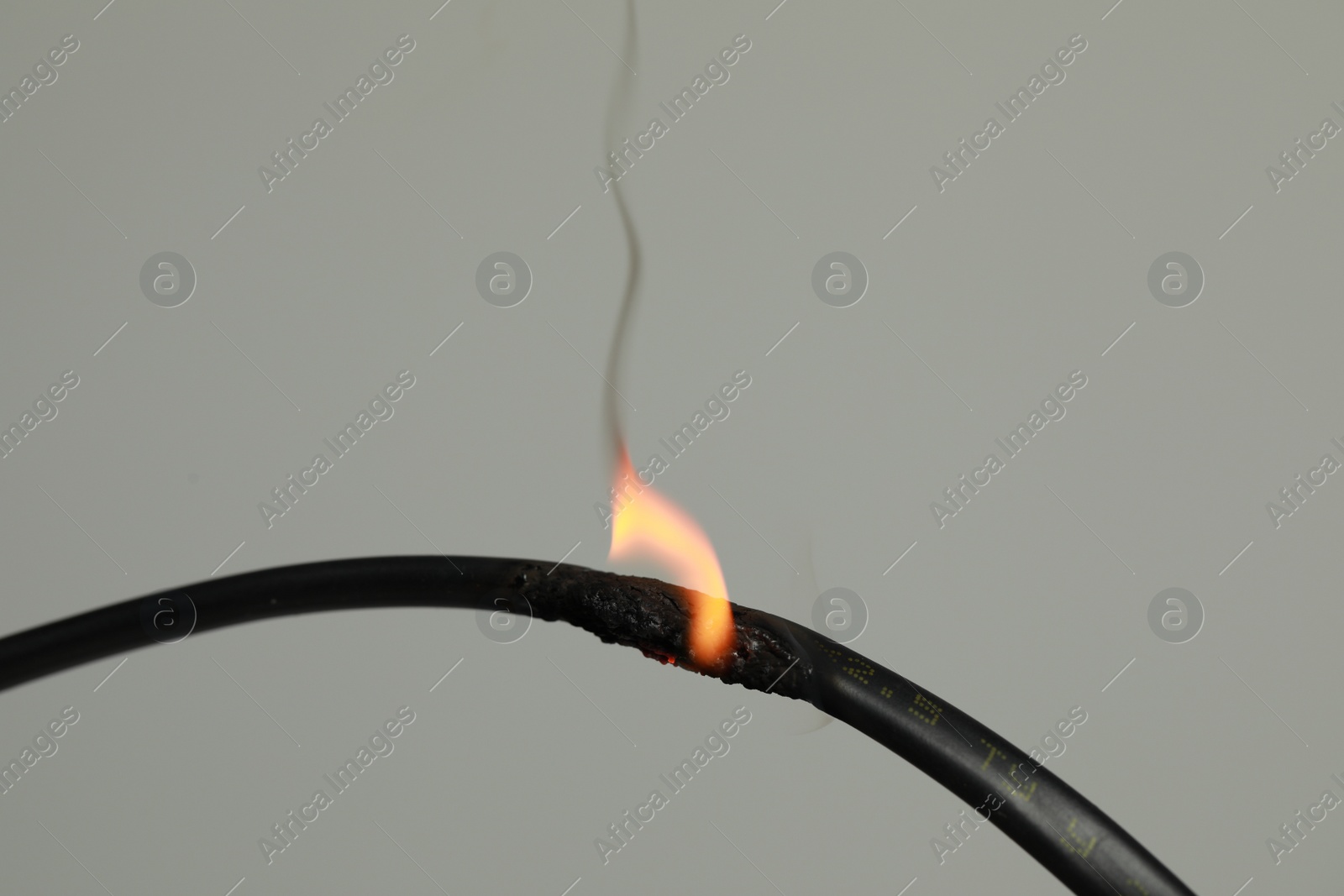 Photo of Inflamed black wire on grey background, closeup. Electrical short circuit