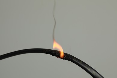 Inflamed black wire on grey background, closeup. Electrical short circuit