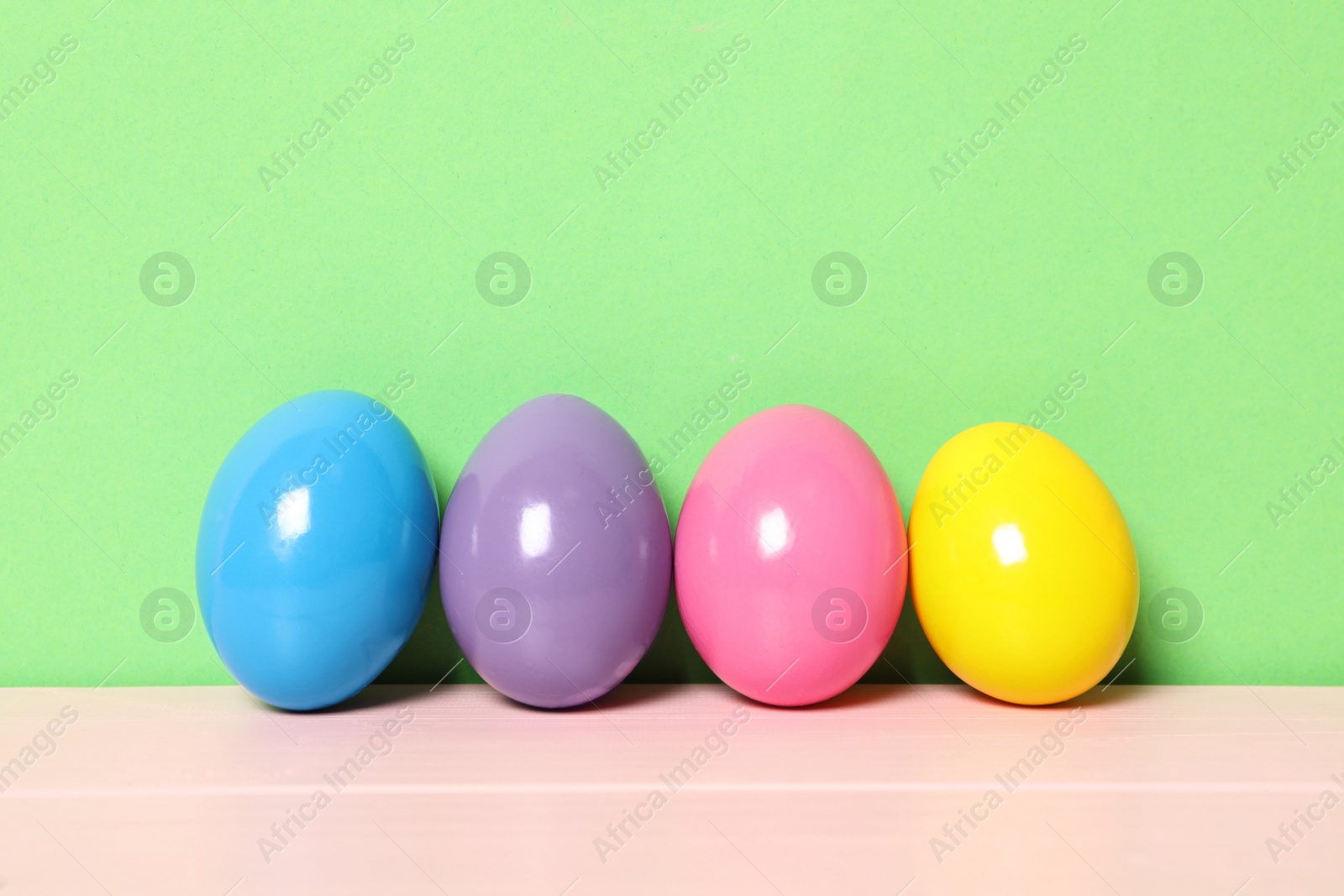 Photo of Easter eggs on pink wooden table against green background, space for text