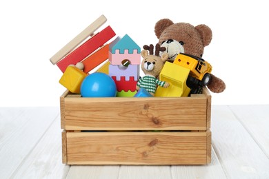 Crate with different children's toys on wooden table against white background