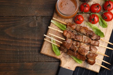 Photo of Tasty cooked marinated meat served with sauce and tomatoes on wooden table, flat lay. Space for text