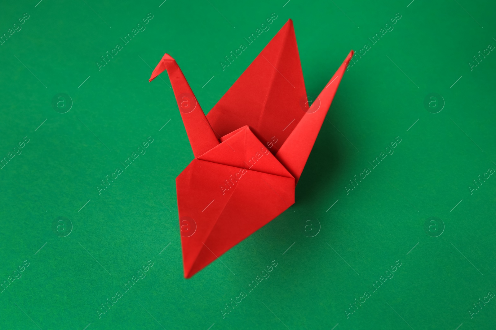 Photo of Red paper origami crane on green background