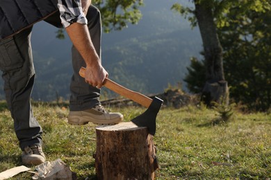 Man with axe cutting firewood outdoors, closeup