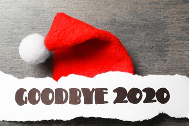 Paper sheet with text Goodbye 2020 and Santa hat on grey background, flat lay