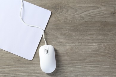 Photo of Wired mouse and mousepad on wooden table, top view. Space for text
