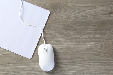 Wired mouse and mousepad on wooden table, top view. Space for text