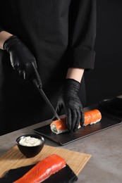 Chef in gloves cutting sushi roll at grey table, closeup